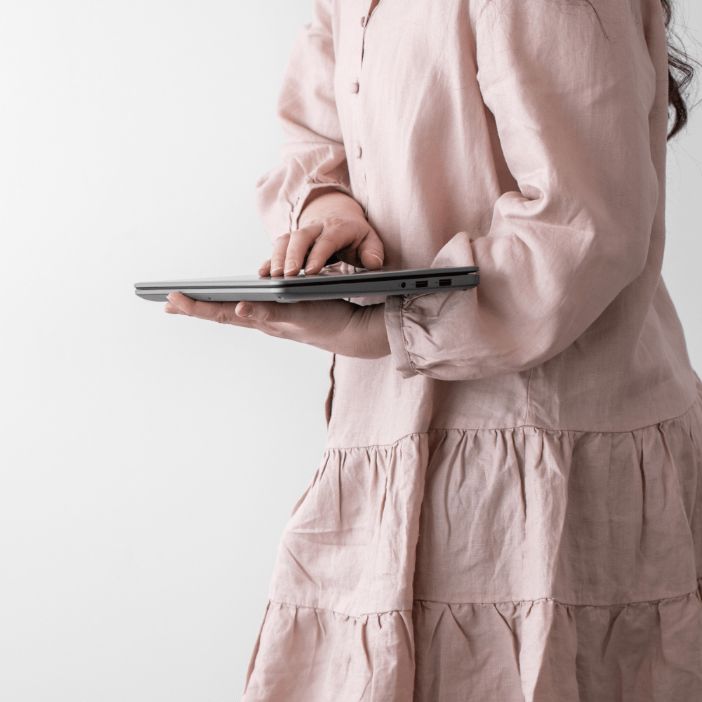 Woman holding a closed laptop in a pink dress.