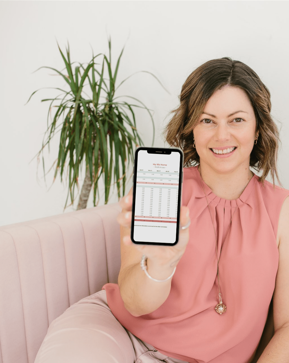 Lisa Turner, a Bookkeeper from Accounted For You, sitting on a pink couch smiling and holding a phone containing an image of free bookkeeping resources.