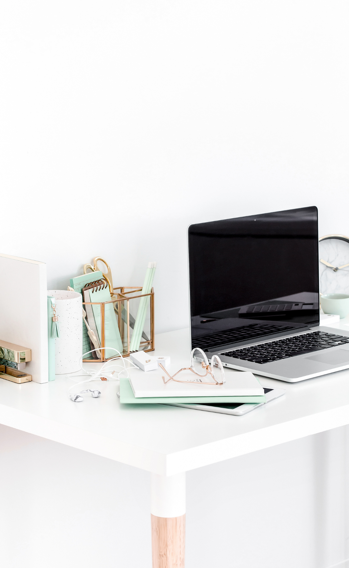 White desk and background with mint and white accessories and silver laptop