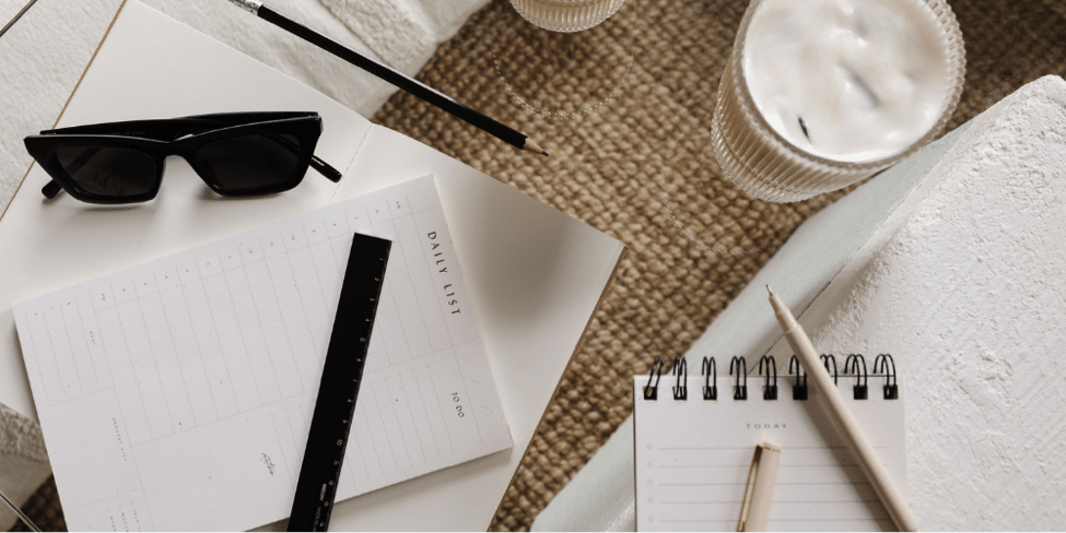 Daily list notebook with sunglasses, pencils, ruler and glass of coffee sitting on a sisal mat