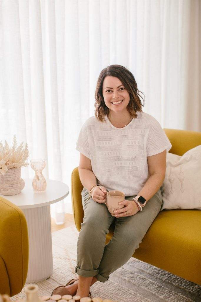 Lisa Turner from Accounted For You - Xero bookkeeper in a white top, sitting on a mustard couch, holding a coffee, next to a white coffee table.