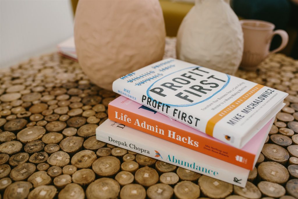 3 books stacked on a coffee table titled profit first life admin hacks and abundance.