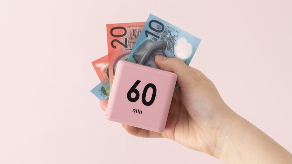 Hand holding pink 60m cube timer with money notes behind.