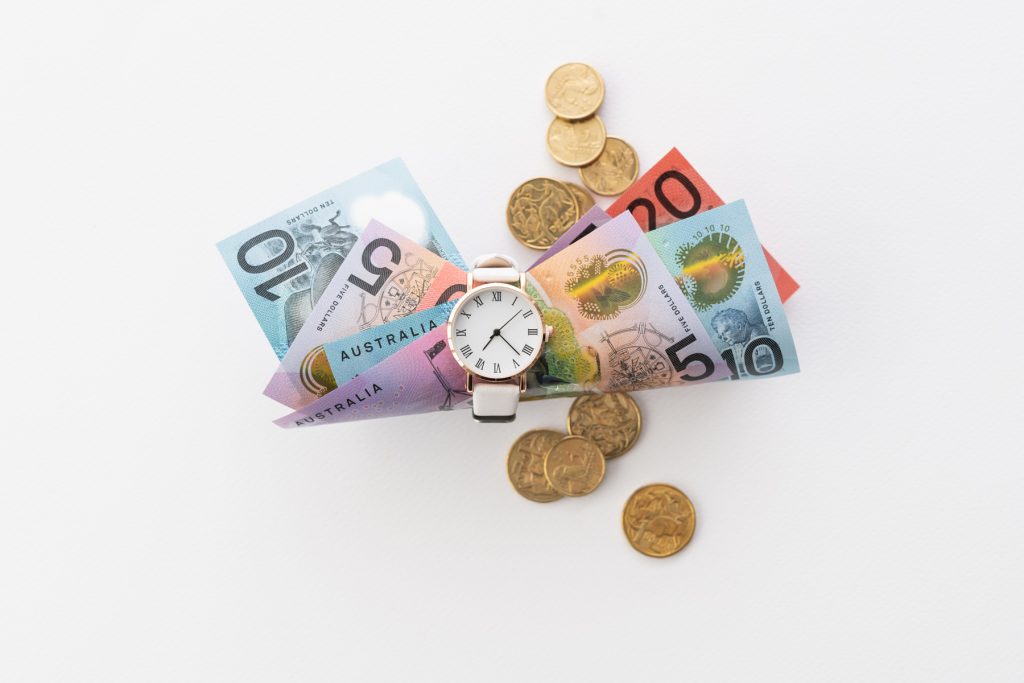 A white watch holding a bunch of Australian currency (notes) with some gold coins scattered on the table. 